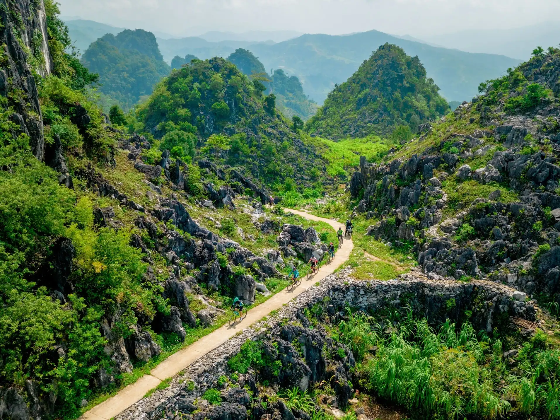 Cyclists on a scenic mountain trail through limestone peaks in northern Vietnam.