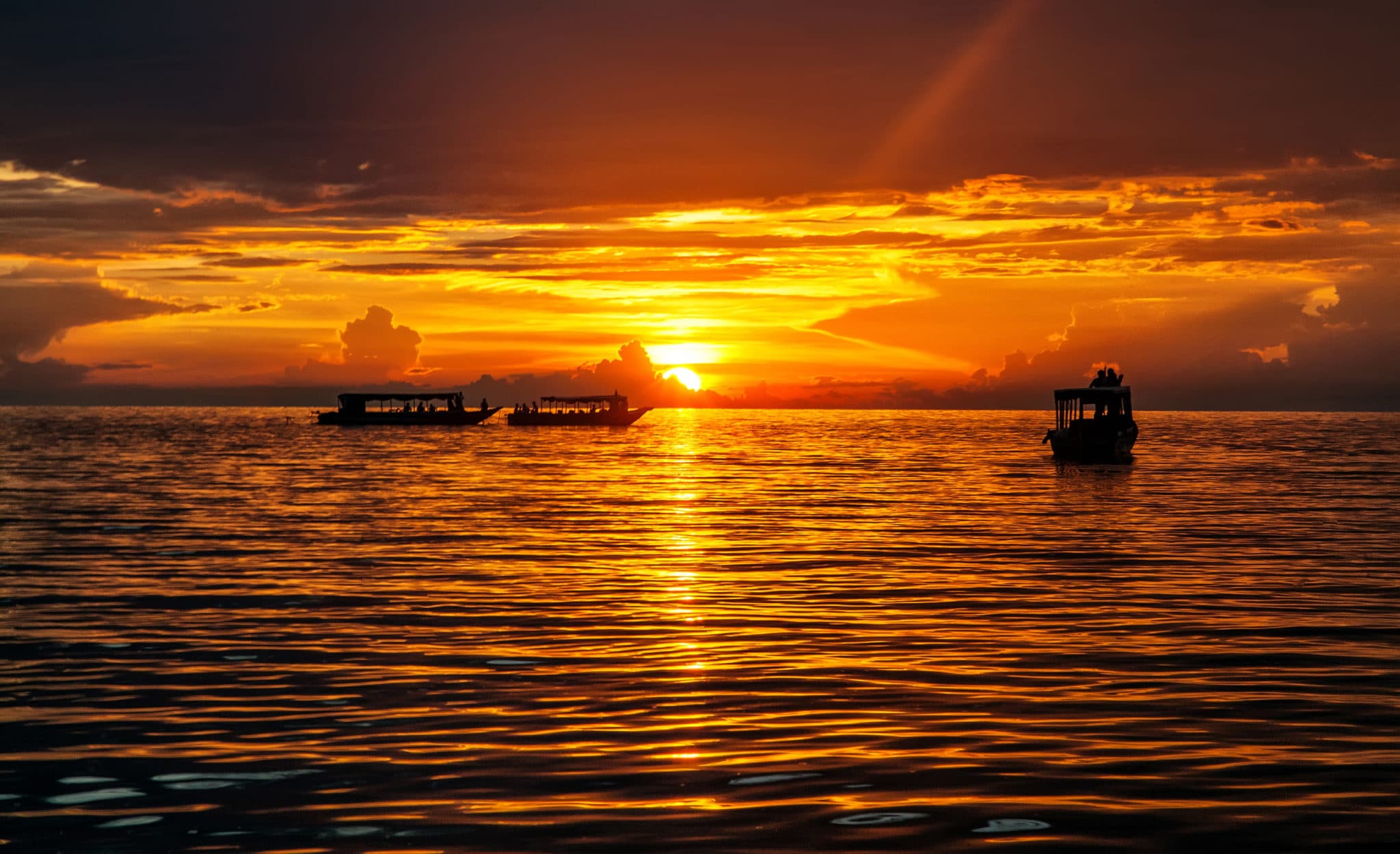 Boats cruising at sunset on Tonle Sap Lake, with golden skies reflecting on the tranquil water.
