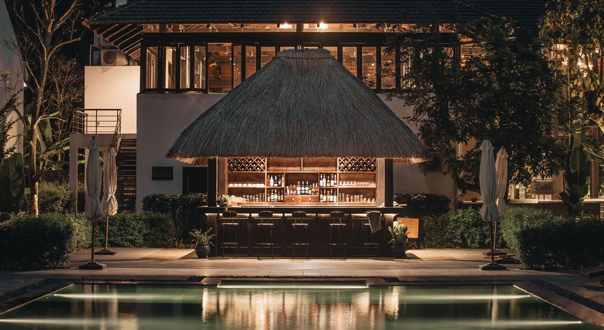 Evening view of Chili Bar at Aravinda Resort Ninh Binh, featuring thatched roof, poolside ambiance, and elegant selection of drinks.