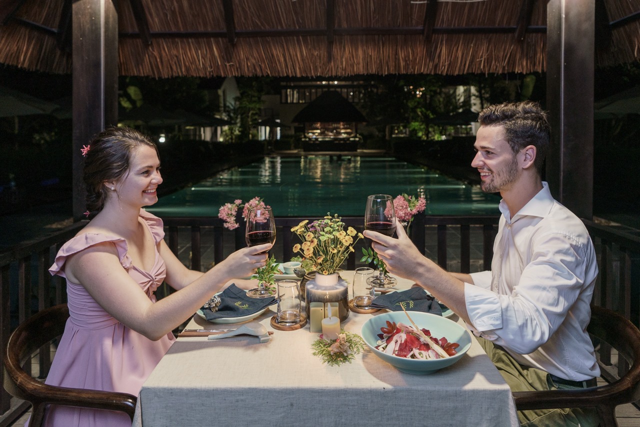 Romantic candlelit dinner by the pool at Aravinda Resort Ninh Binh, with couple toasting wine, elegant setup, and intimate atmosphere.