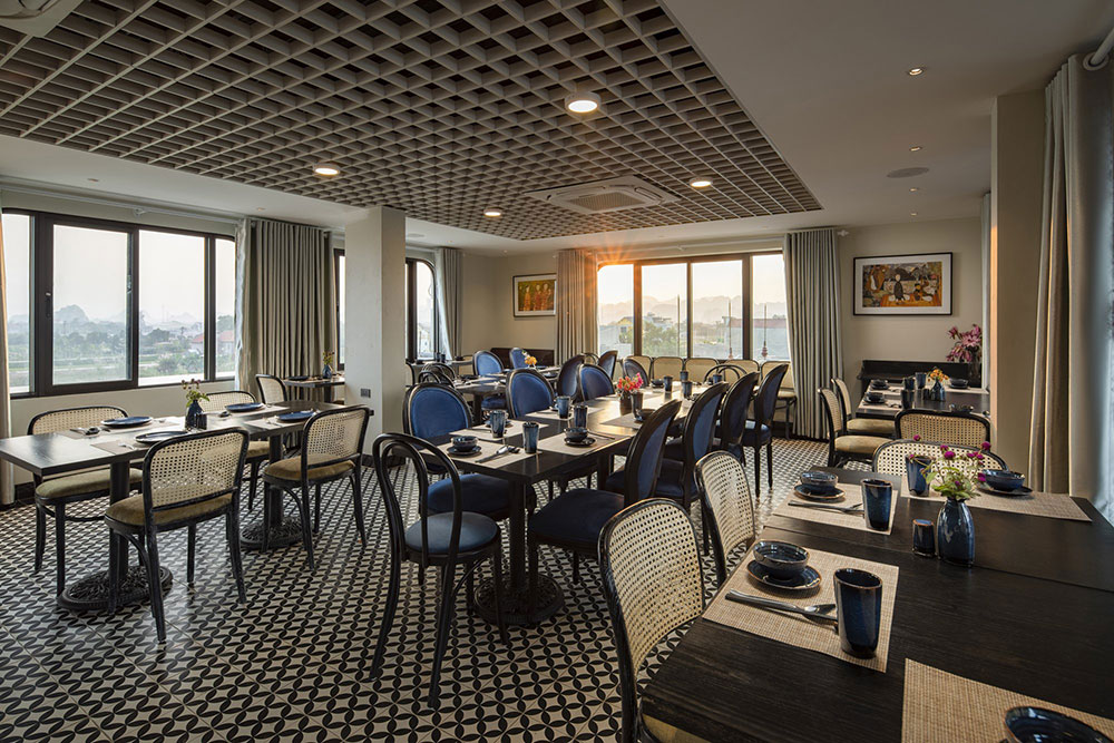 Elegant dining room at lalita boutique hotel featuring modern furniture, panoramic windows, patterned floor tiles, and cozy sunset ambiance in Ninh Binh.