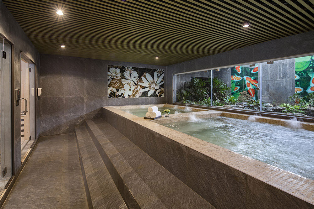 Relaxing indoor jacuzzi at lalita boutique hotel featuring warm lighting, floral mural, stone walls, and garden view through glass window.