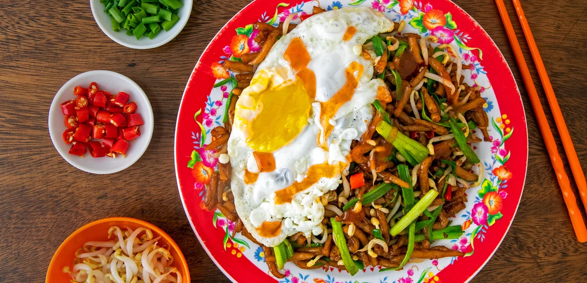 A sizzling plate of Lort Cha, stir-fried pin noodles with vegetables, a popular Cambodian cuisine street food