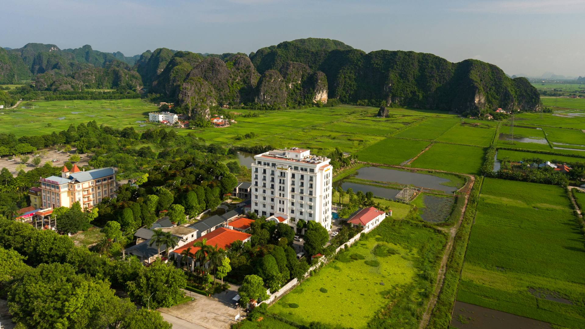 Aerial view of Ninh Binh Hidden Charm Hotel & Resort surrounded by lush rice fields and limestone mountains in Tam Coc.
