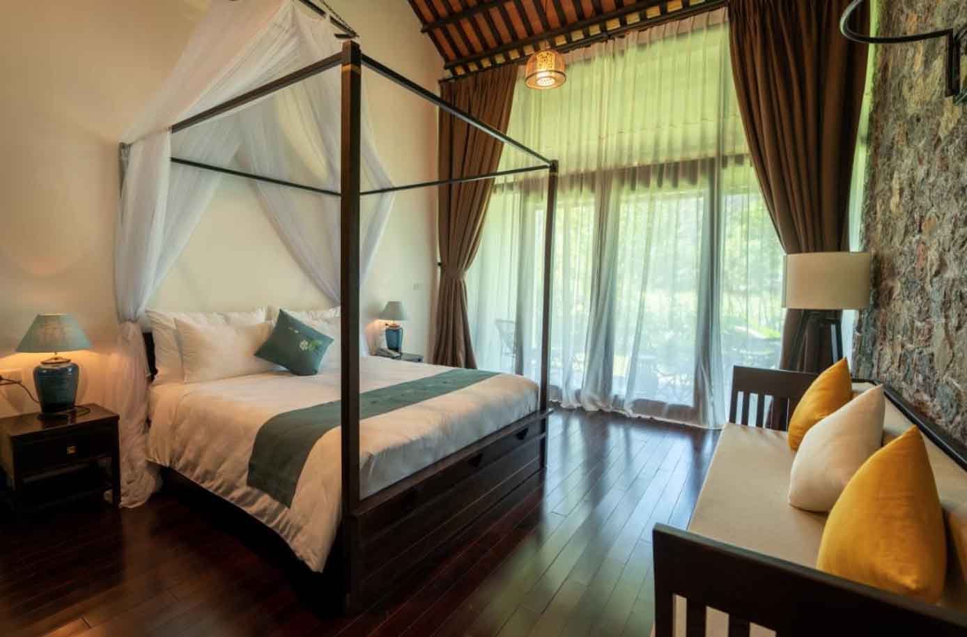 Spacious Countryside Deluxe at Aravinda Resort Ninh Binh, featuring stone wall accents, canopy bed, elegant decor, and serene garden views.