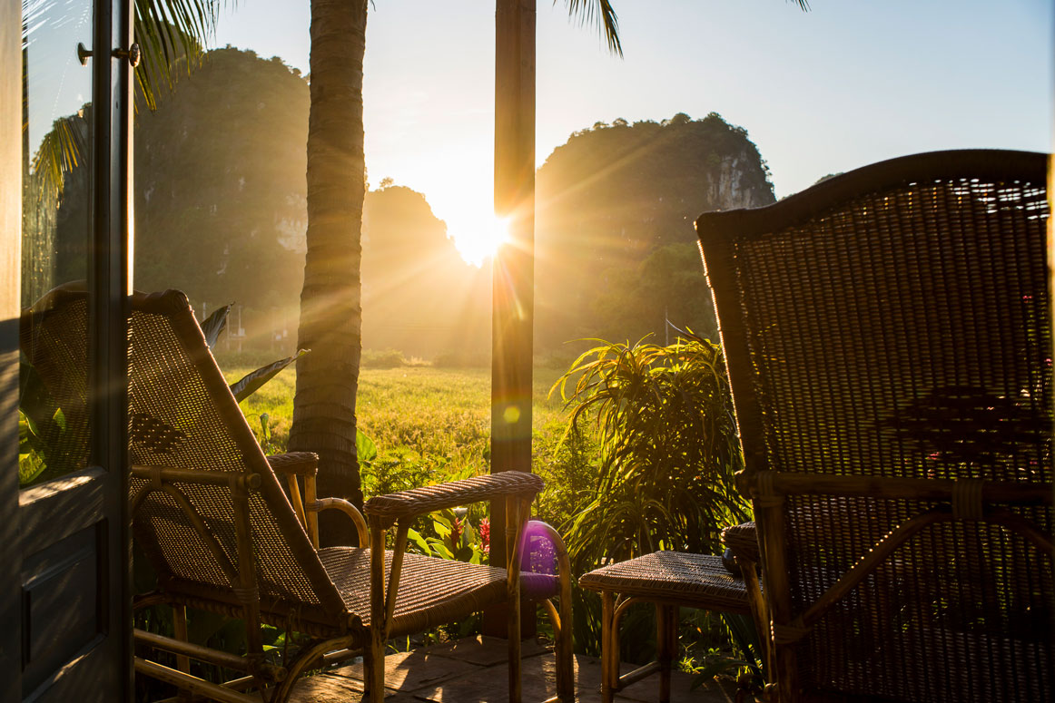 Sunset view from Tam Coc Garden Resort balcony with bamboo chairs overlooking rice fields and limestone mountains.