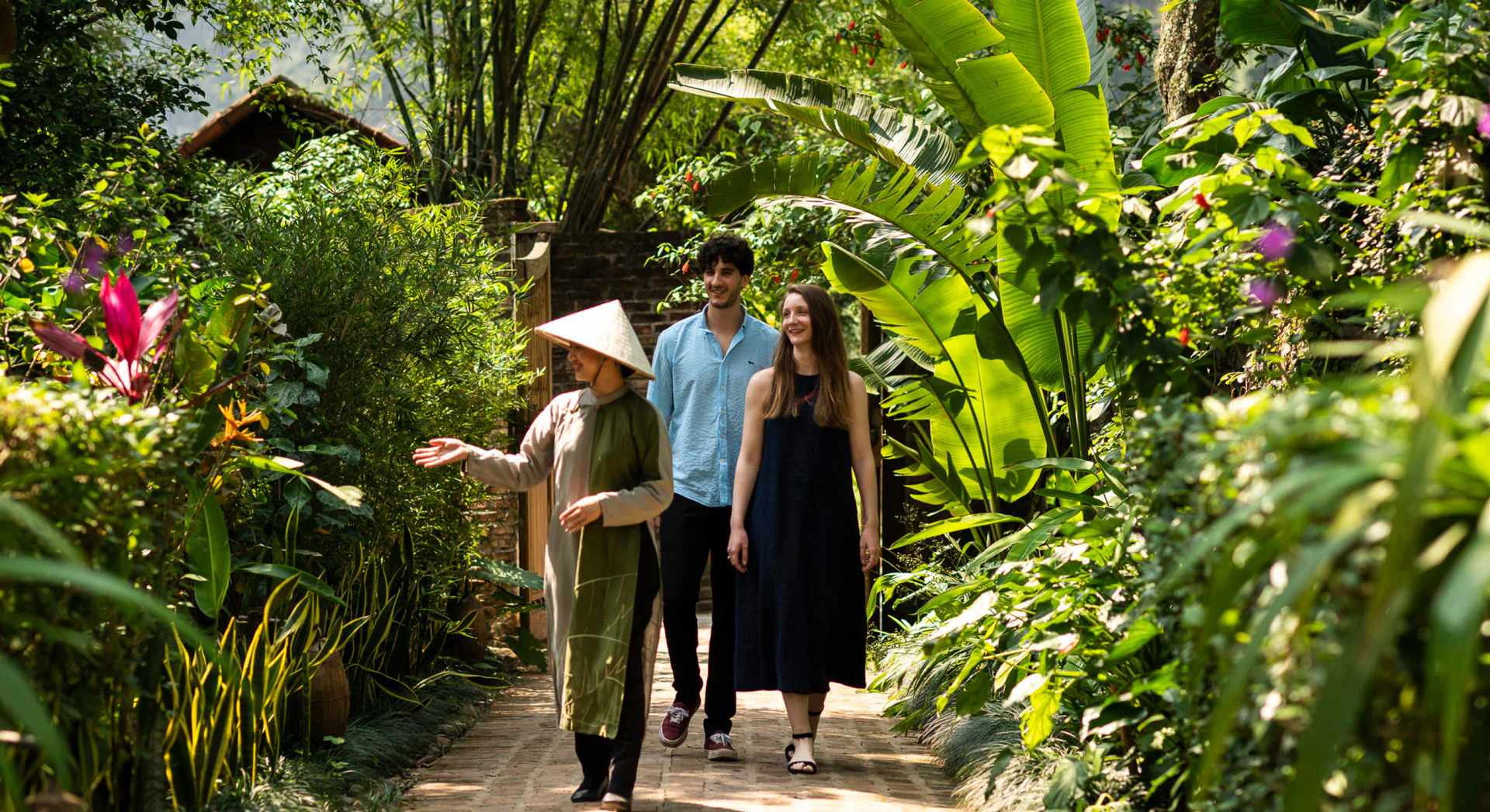 Guests walking through lush gardens at Tam Coc Garden Resort with a local guide in a traditional hat.
