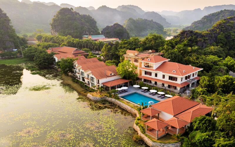 Peaceful lakeside scene at Tam coc la montagne resort & spa with blooming lotus flowers and charming white villas under mountains.