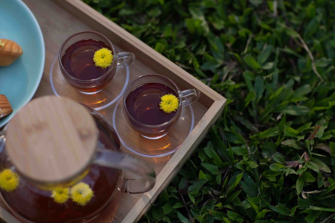 Afternoon tea at Aravinda Resort Ninh Binh, featuring herbal chrysanthemum tea served in glass cups with homemade pastries outdoors.