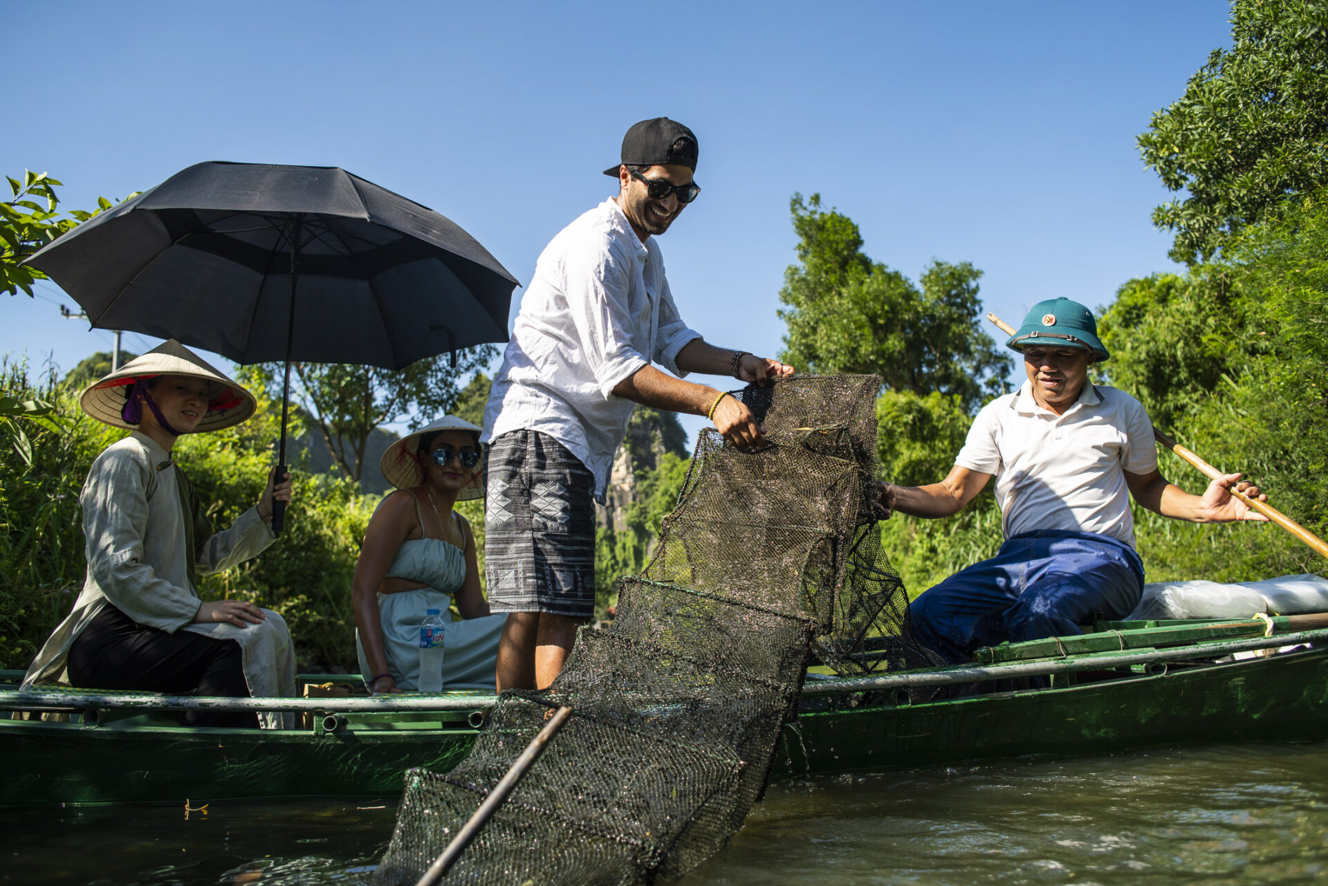Guests from Tam Coc Garden Resort joining locals on boat fishing experience in Ninh Binh river under sunlight.
