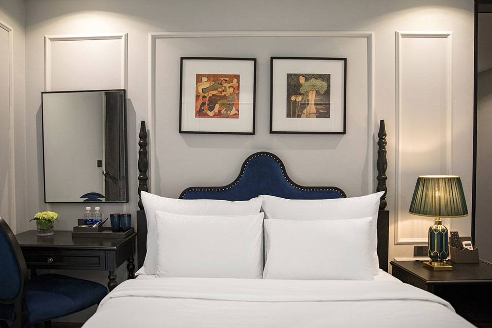 legant bedroom at lalita boutique hotel decorated with blue velvet chair, paintings, bedside lamps, and minimalist Indochine design.

