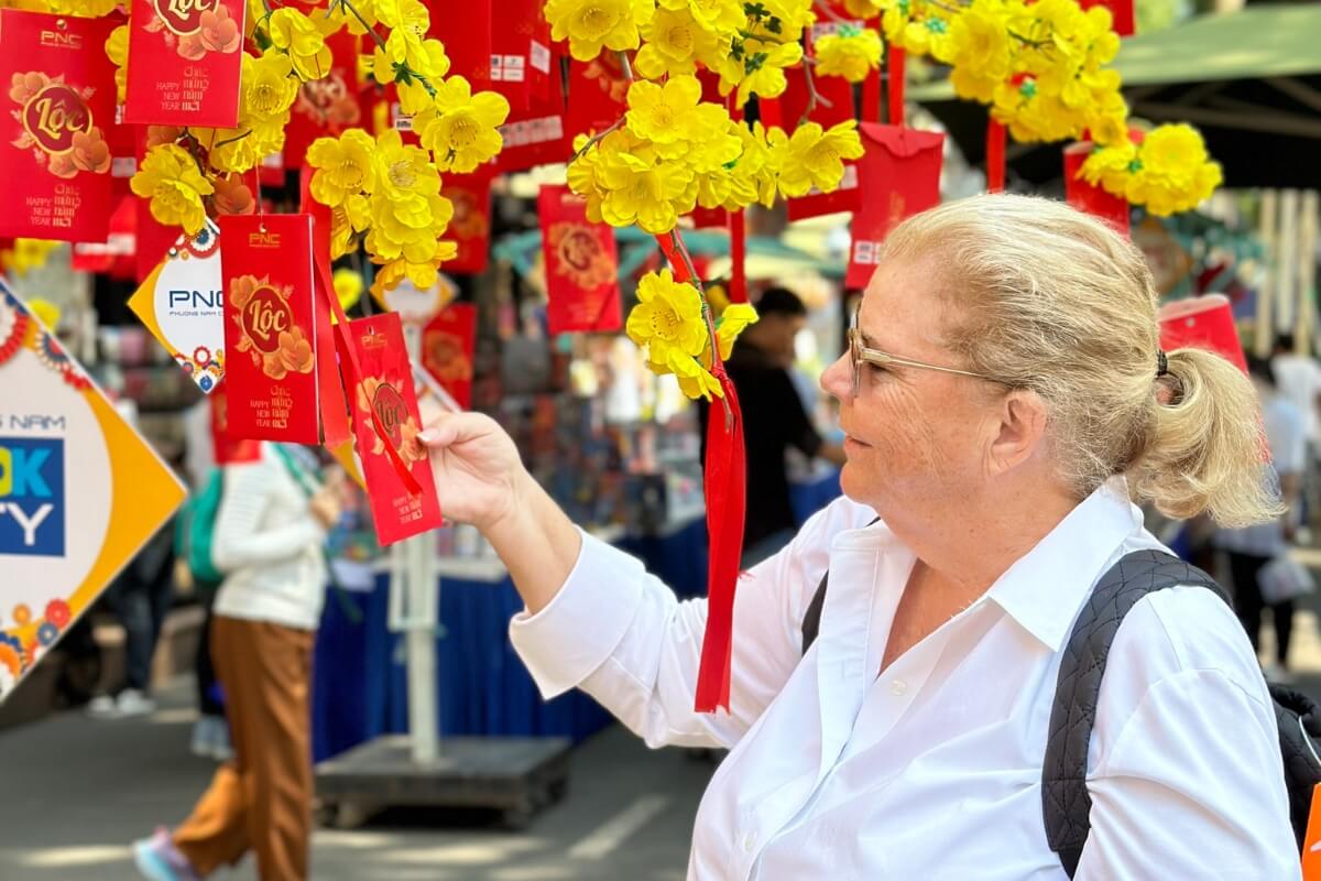Tourist enjoying Vietnamese New Year’s market with lucky envelopes and blossoms, exploring culture and Vietnamese New Year’s Food traditions.