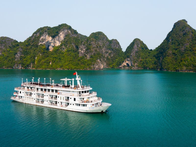 A luxurious white cruise ship sails on the emerald waters of Ha Long Bay, an ideal getaway in Vietnam in October