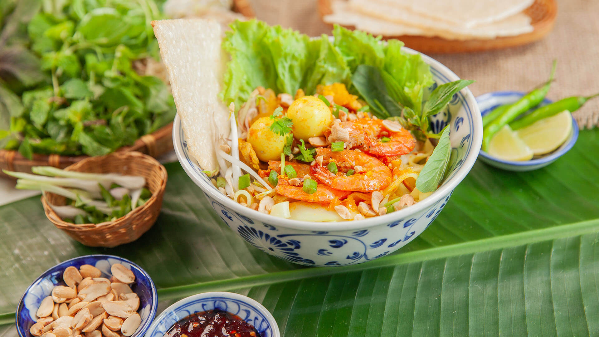 A colorful bowl of mi quang, a signature Vietnam street food with shrimp, quail eggs, herbs, peanuts, and rice noodles.