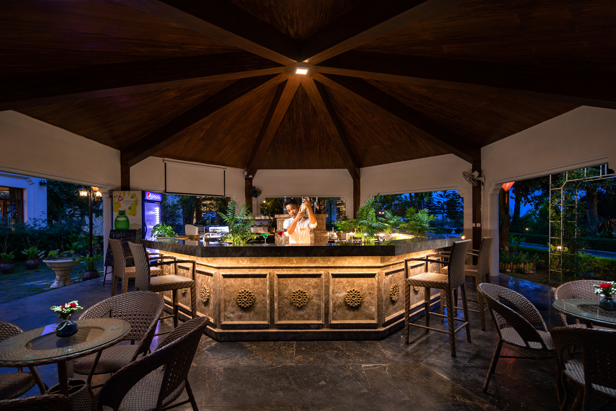 Outdoor bar at Ninh Binh Hidden Charm Hotel & Resort with bartender preparing cocktails in a relaxing tropical setting.