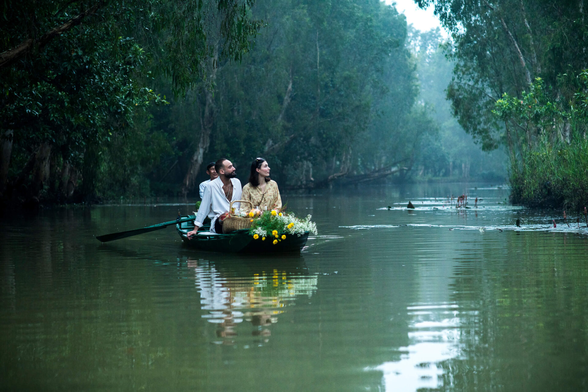 Guests from Tam Coc Garden Resort enjoying peaceful boat ride on river surrounded by lush green forest.