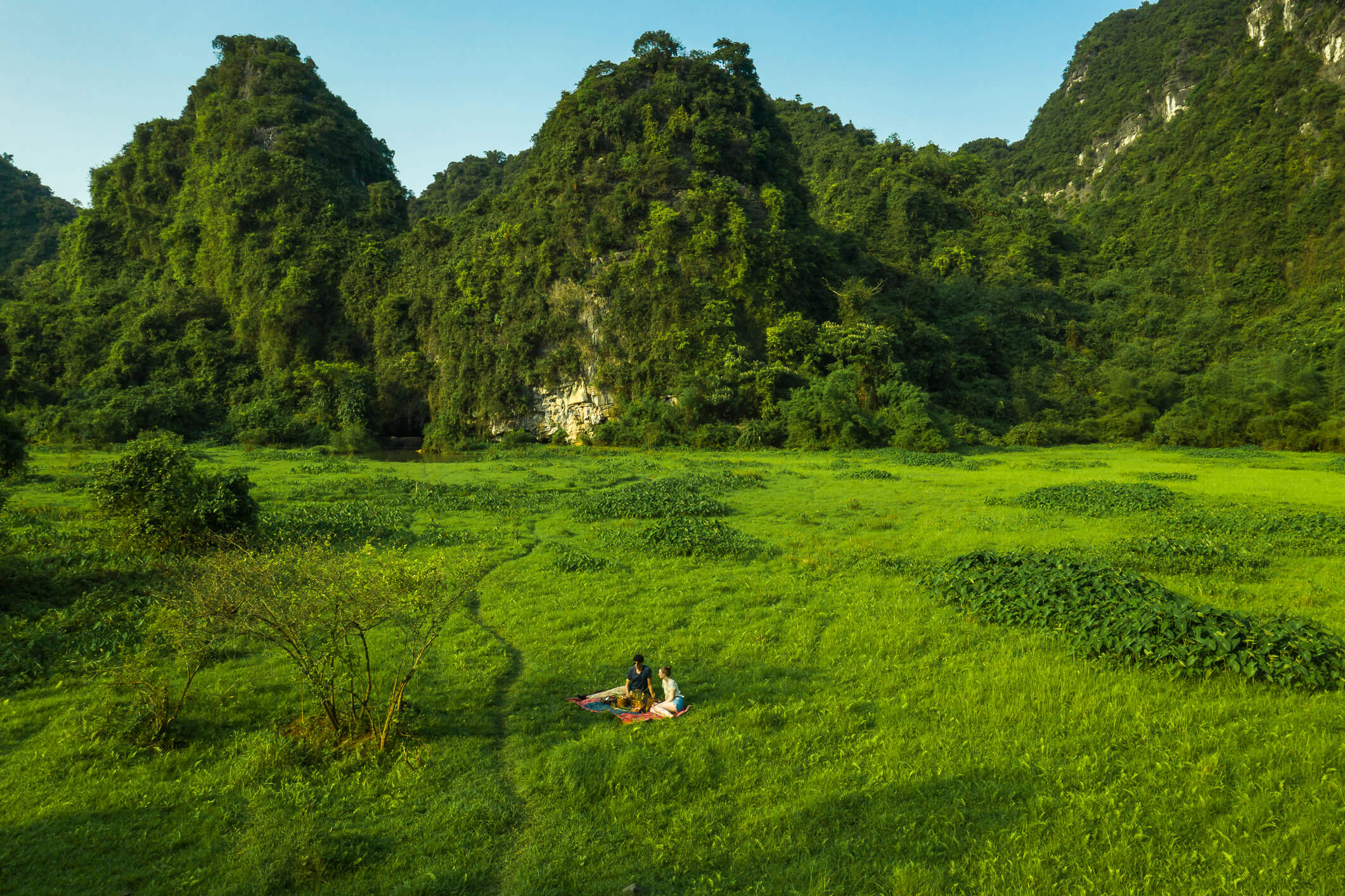 Couple enjoying picnic in green valley near Tam Coc Garden Resort surrounded by limestone mountains and nature.