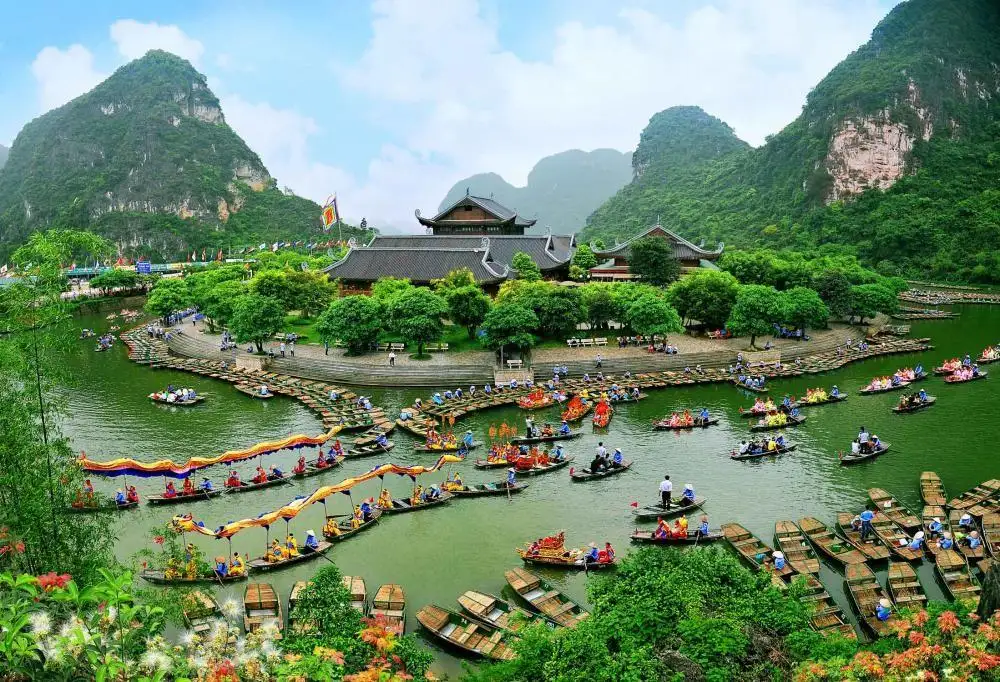 Colorful boats and tourists exploring Trang An near Tam Coc La Montagne Resort & Spa, surrounded by limestone mountains and lush greenery.