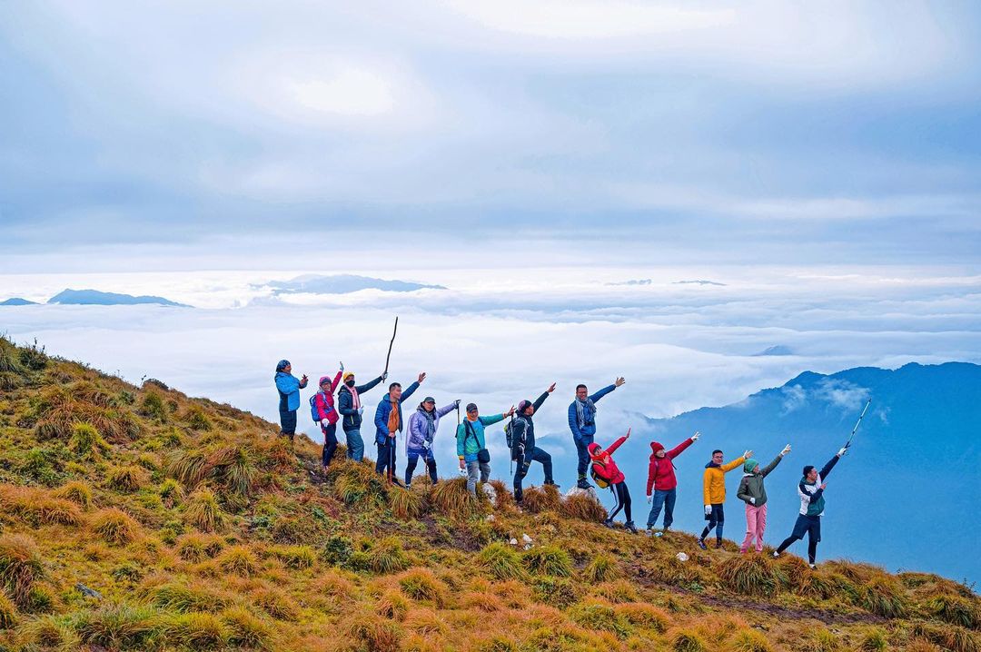 Trek Mu Cang Chai group celebrating on a mountain edge overlooking clouds. Great scenery for Vietnam in November hiking