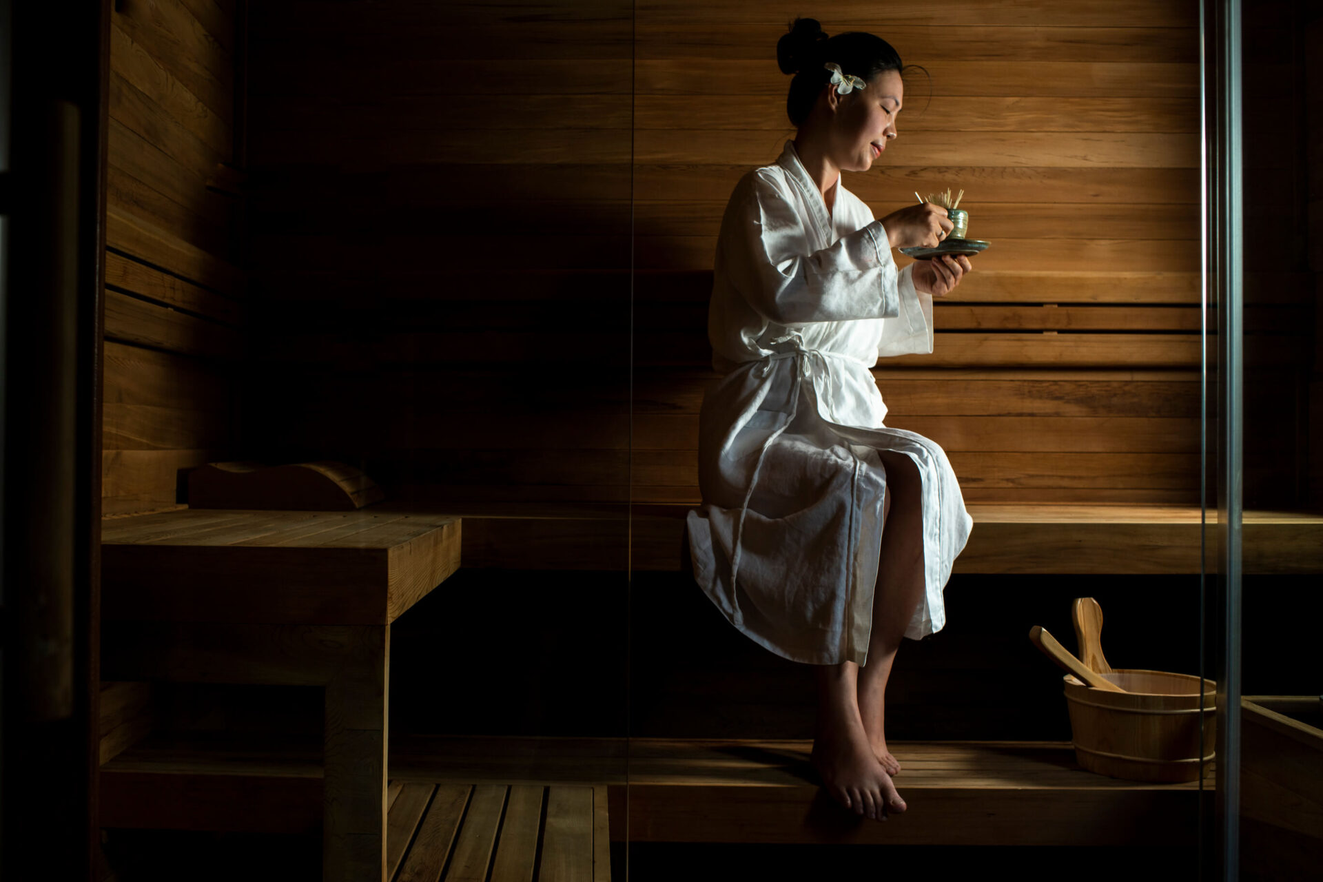 Guest relaxing in wooden sauna at Sati Spa, Tam Coc Garden Resort, wearing robe and holding herbal tea.