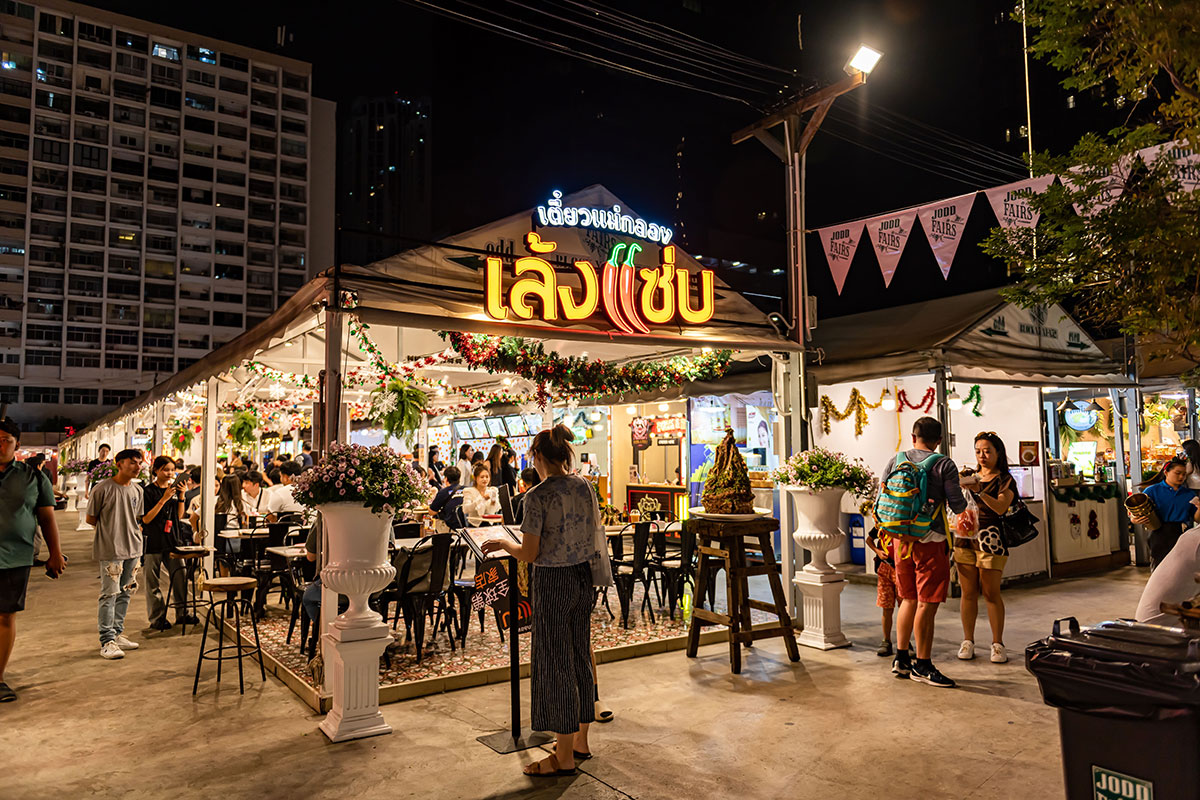A busy, well-lit food stall and dining area at Jodd Fairs, a popular Bangkok night market