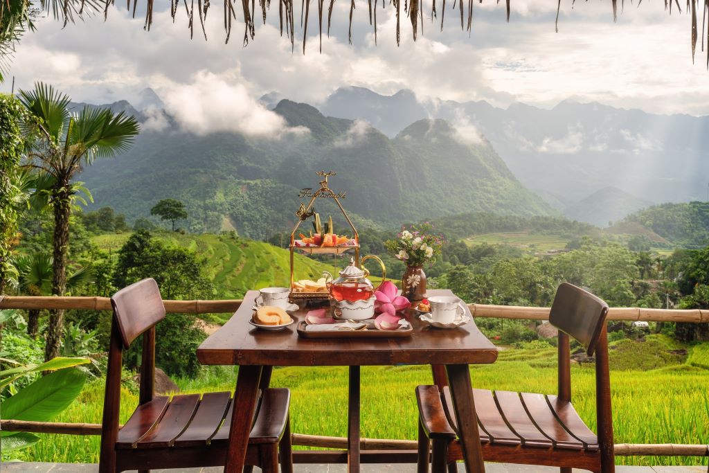Tea set and snacks on a wooden table overlooking misty mountains and vibrant green rice terraces at Pu Luong Retreat