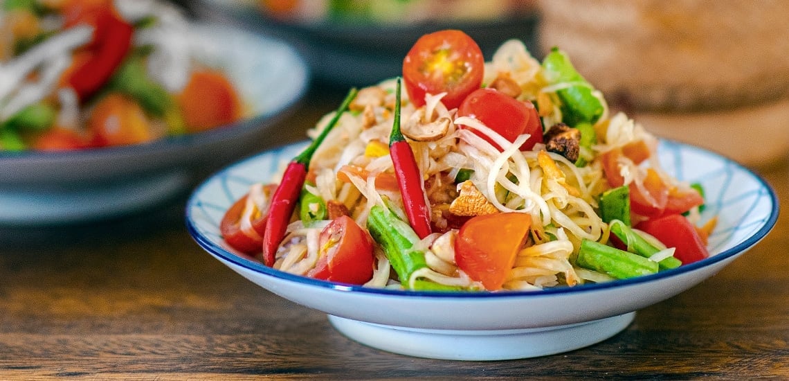 Close-up of a plate of spicy Som Tam (papaya salad), a popular street food at a Bangkok night market
