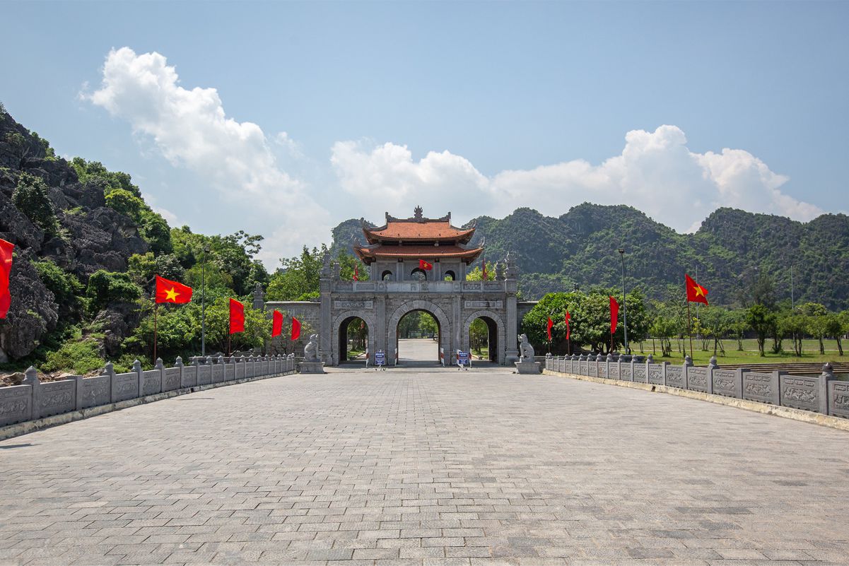 Hoa Lu, framed by lush green mountains and red Vietnamese flags, signifying the historical depth of Vietnam culture