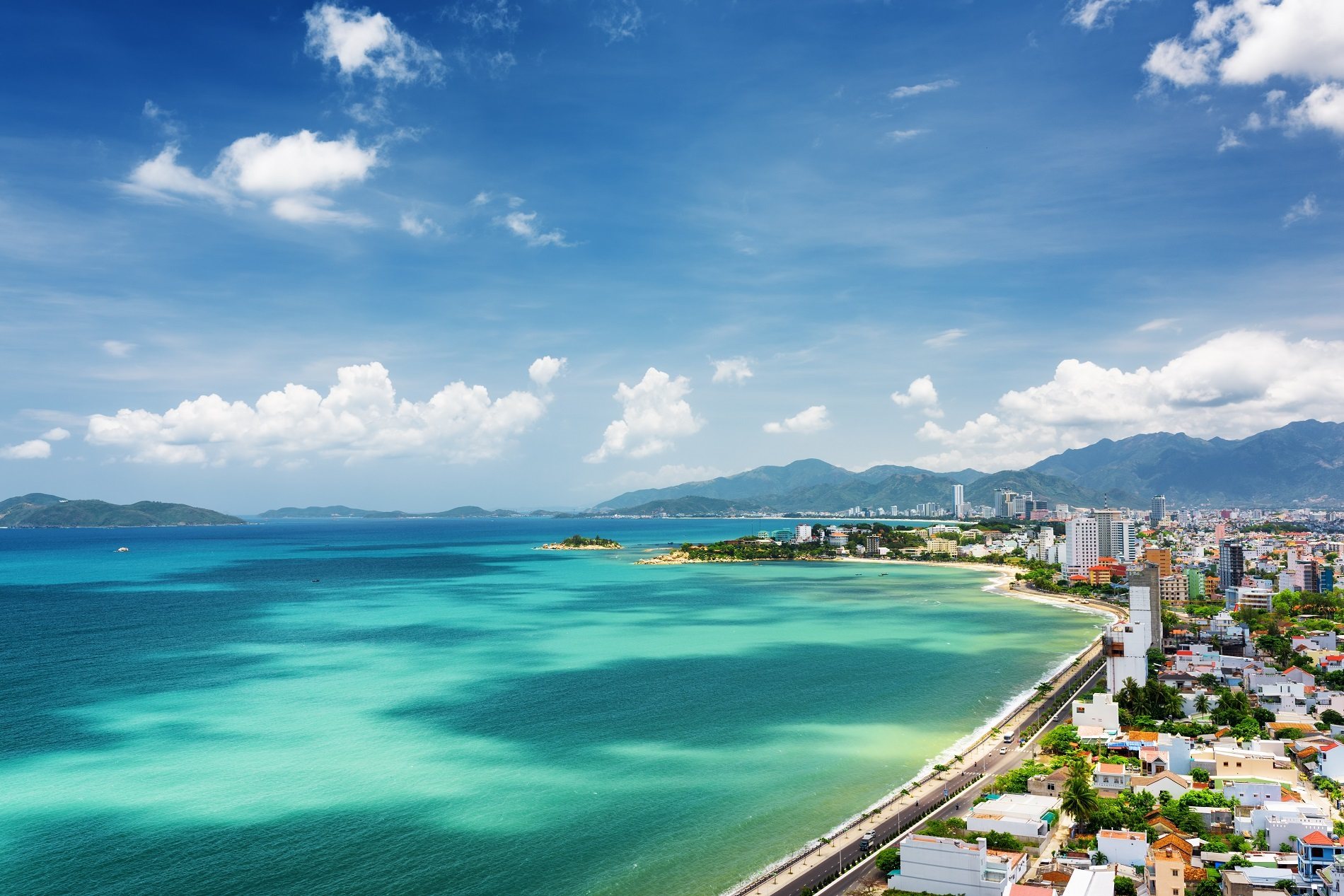 An aerial view of a pristine, narrow sandbar extending into the clear turquoise water near a lush island, exemplifying the best beaches in nha trang vietnam