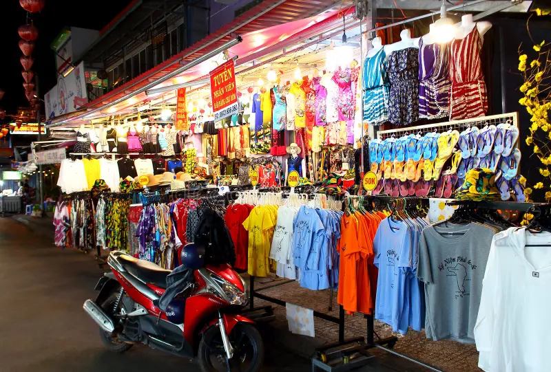 Vibrant stall at Phu Quoc night market selling colorful clothing, including T-shirts with "Phu Quoc" prints