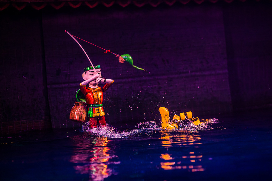 A single male water puppet, fishing with a pole while standing in the water during a Hanoi water puppet show