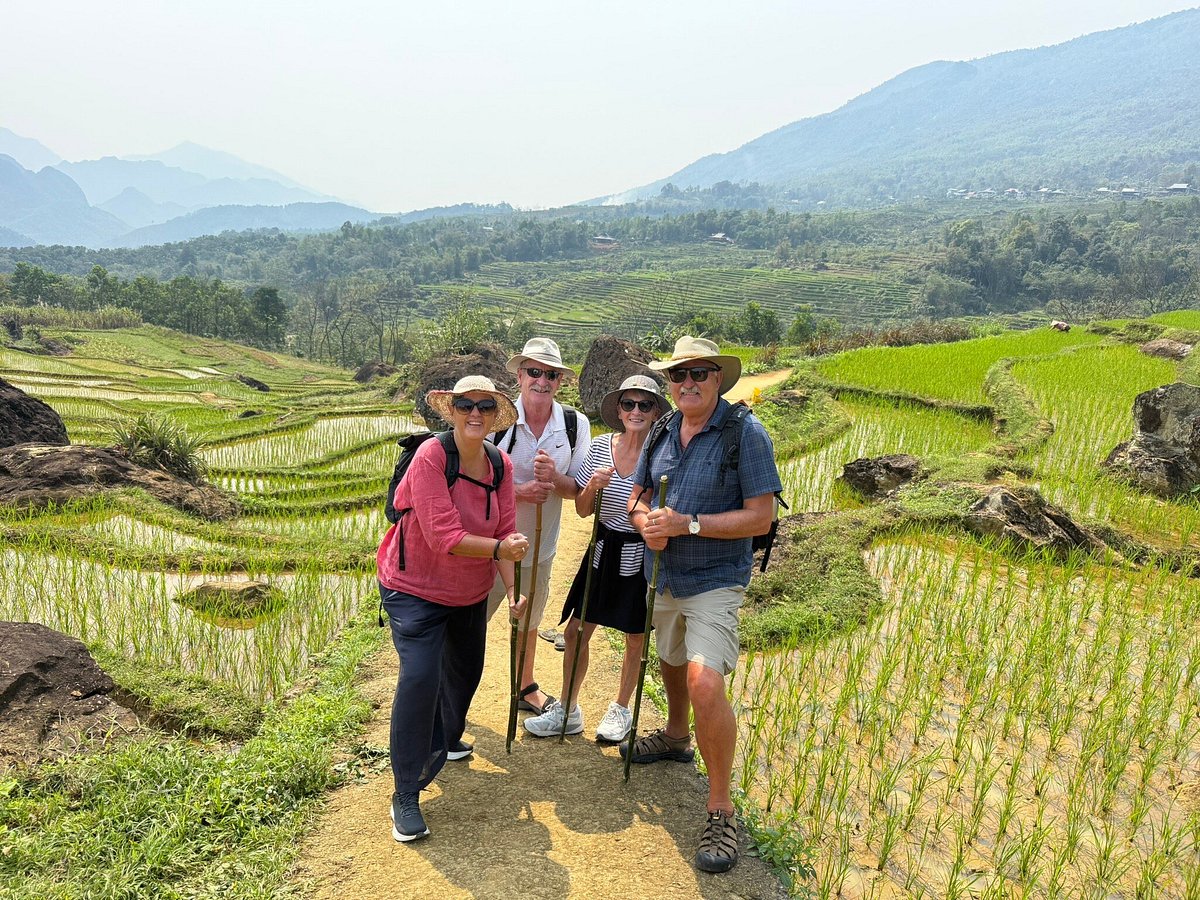 Four happy trekkers with hiking poles posing on a dirt path next to rice paddies near Pu Luong Retreat