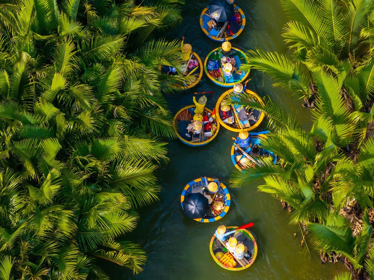 Colorful basket boats glide through lush waterways of Bay Mau Coconut Forest under bright tropical sunlight.