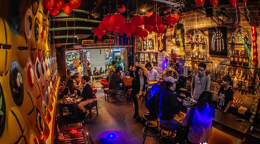 Funky Buddha Bar: Cozy and uniquely decorated bar interior with red lanterns, exposed brick walls, and patrons enjoying drinks at the counter and tables.