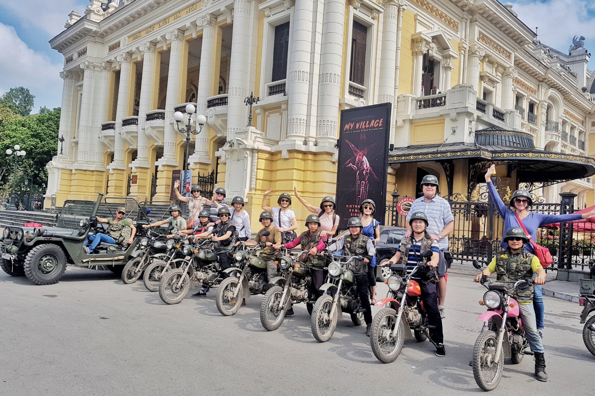 A group of tourists wearing helmets posing on vintage motorbikes and a military jeep in front of the Hanoi Opera House, representing "hanoi day tours”