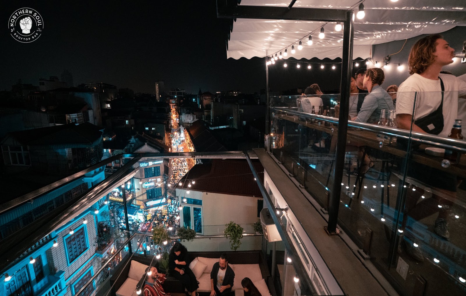 Northern Soul Rooftop Bar: Night view from a rooftop bar in Hanoi's Old Quarter, showing patrons enjoying the city skyline and street traffic below.
