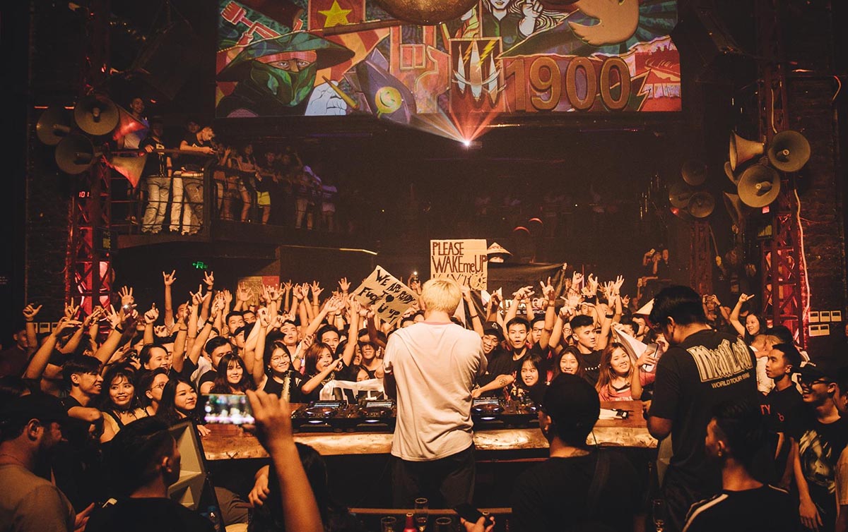 The Soundtrack of the Street: Live Music: Crowded nightclub or bar scene with a DJ performing on stage and the audience cheering, capturing the vibrant nightlife soundtrack.