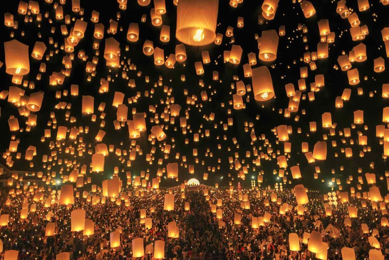 Loy Krathong and Yi Peng Festivals: Thousands of illuminated sky lanterns (khom loi) floating into the night sky over a crowd, capturing the spectacular sight of the Yi Peng festival.