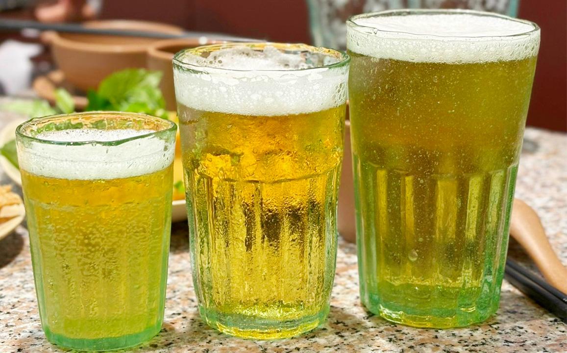 Savoring Ta Hien Street Draft Beer: Close-up of three glasses of chilled Vietnamese draft beer (Bia Hơi) with foam, a signature experience on Ta Hien Street
