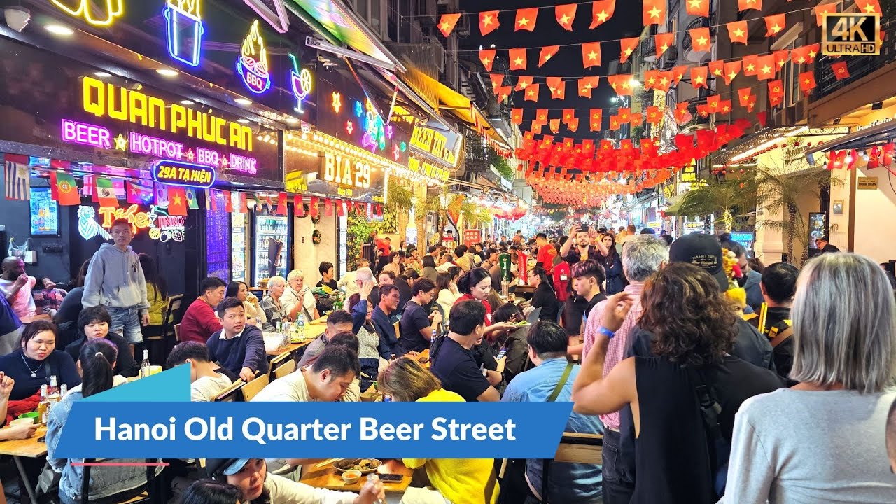 Operating Hours of Beer Street Hanoi: Lively night scene on Ta Hien Street with tourists and locals enjoying street-side seating under bright neon signs, emphasizing evening hours.