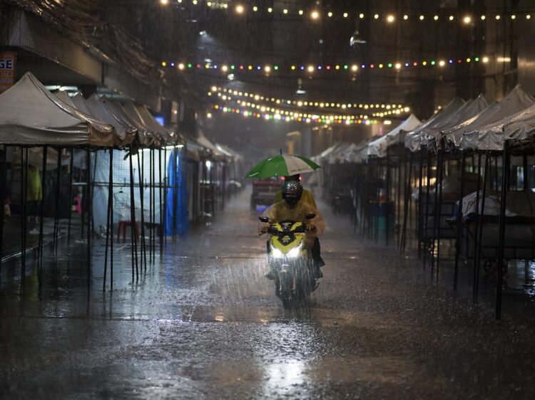 The Rainy Season (July - November): A Quiet and Lush Alternative: Motorbike rider in a poncho and umbrella navigating a wet street at night, capturing the heavy rainfall and quiet atmosphere.