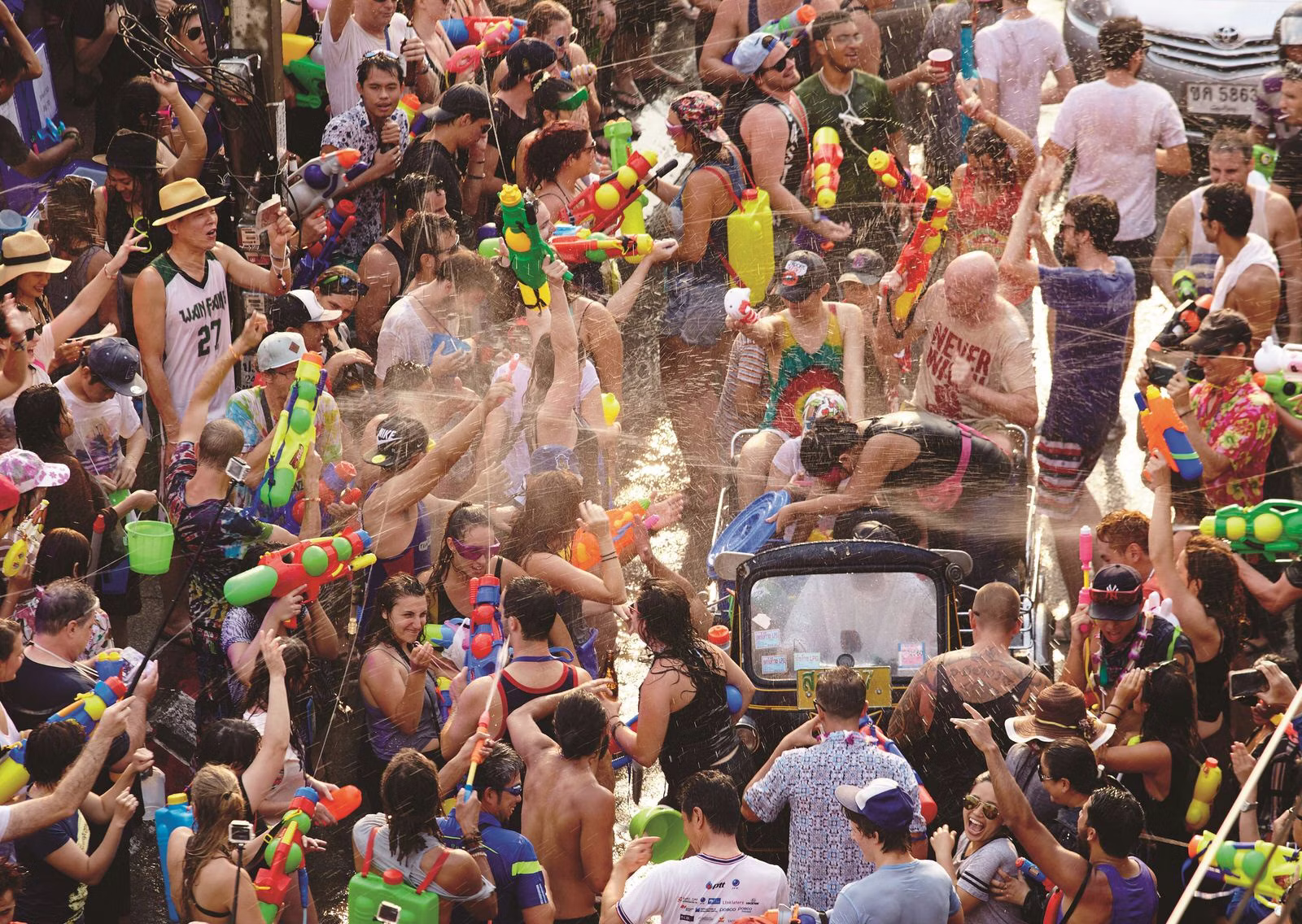 Songkran Festival: Large, crowded street water fight in Thailand, with people holding water guns and buckets, celebrating the traditional Thai New Year holiday.