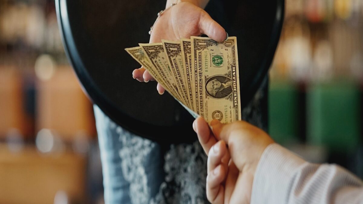 Tipping culture in Vietnam: Close-up of a hand passing US dollar bills, representing payment or an optional tip in the service industry.