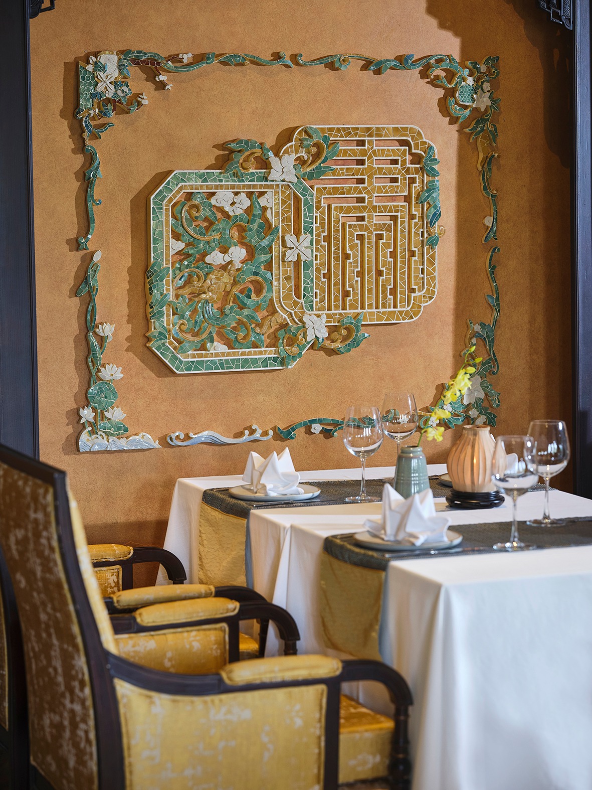 Elegant dining setup at Ancient Hue Garden Houses featuring fine tableware, golden chairs, and intricate imperial-inspired wall décor.