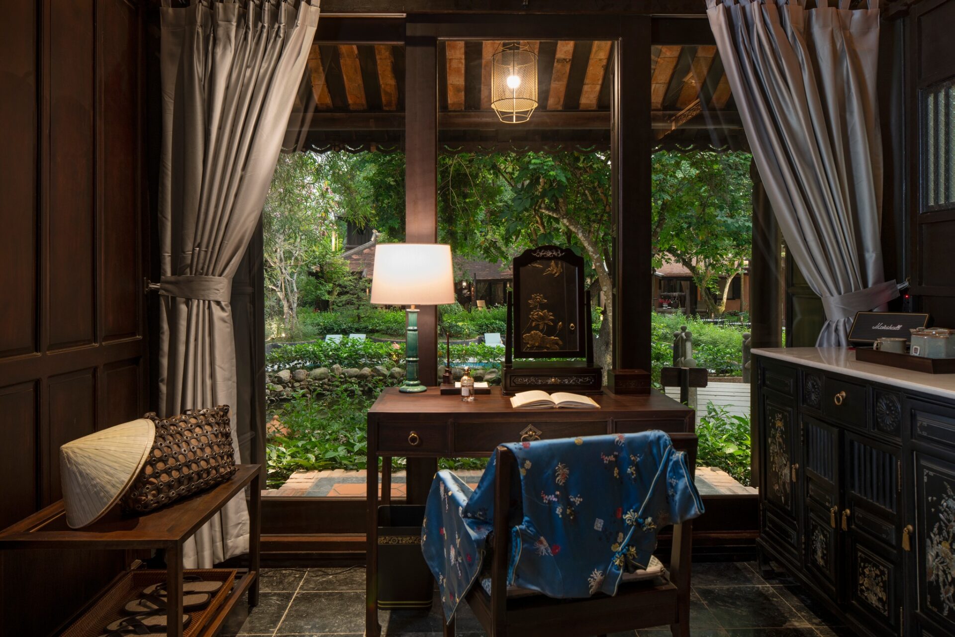 Peaceful study corner at Ancient Hue Garden Houses featuring wooden furniture, silk robe, soft lighting, and lush garden views outside.
