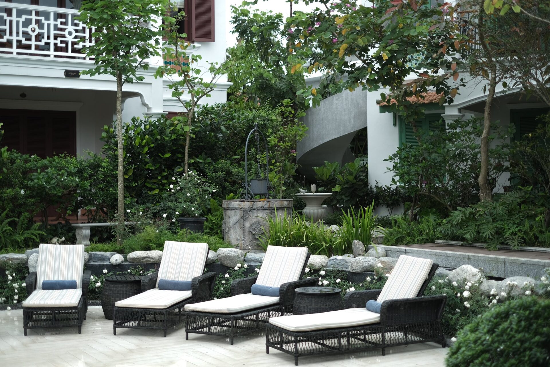 Peaceful garden view at Ancient Hue Garden Houses featuring sun loungers, lush greenery, and elegant French-inspired architecture in a serene courtyard.