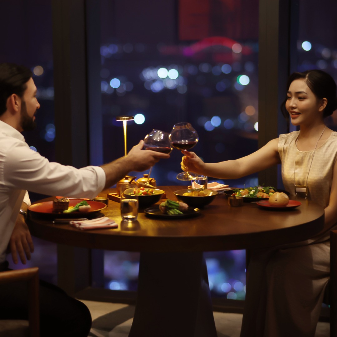 Couple enjoying a romantic dinner at Melia Vinpearl Hue, savoring fine cuisine and wine overlooking Hue’s glittering night lights.
