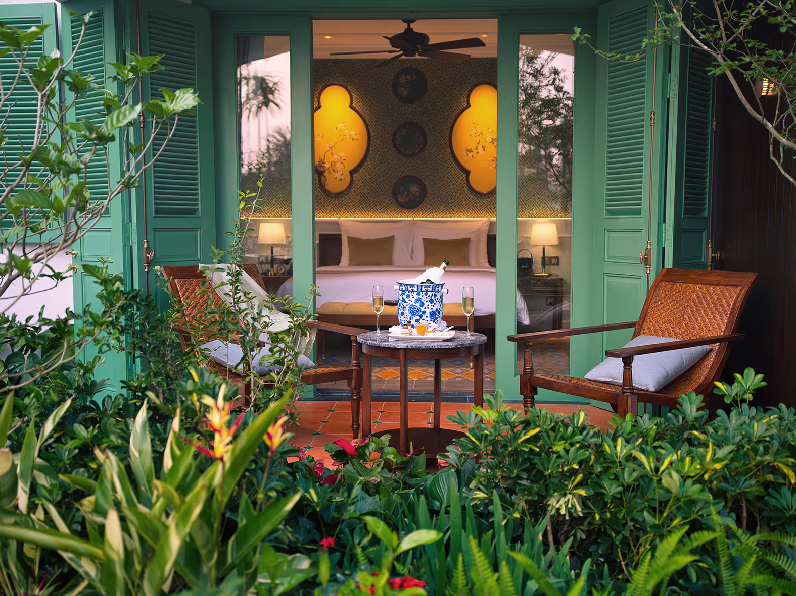 Romantic garden terrace at Ancient Hue Garden Houses with rattan chairs, champagne setup, and lush greenery outside a French-style villa.