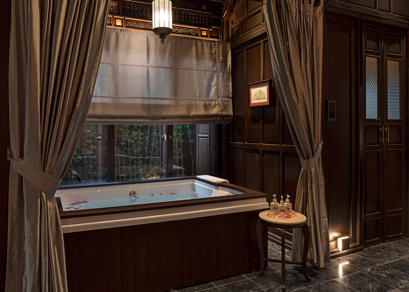 Luxurious bathroom at Ancient Hue Garden Houses featuring a deep bathtub, silk curtains, wooden walls, and romantic ambient lighting.