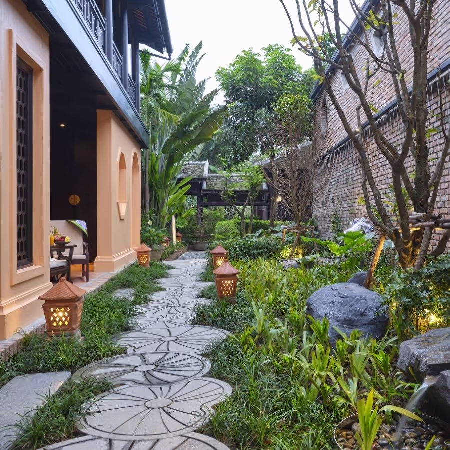 Serene garden path at Ancient Hue Garden Houses illuminated by lanterns, surrounded by lush greenery and traditional architecture.